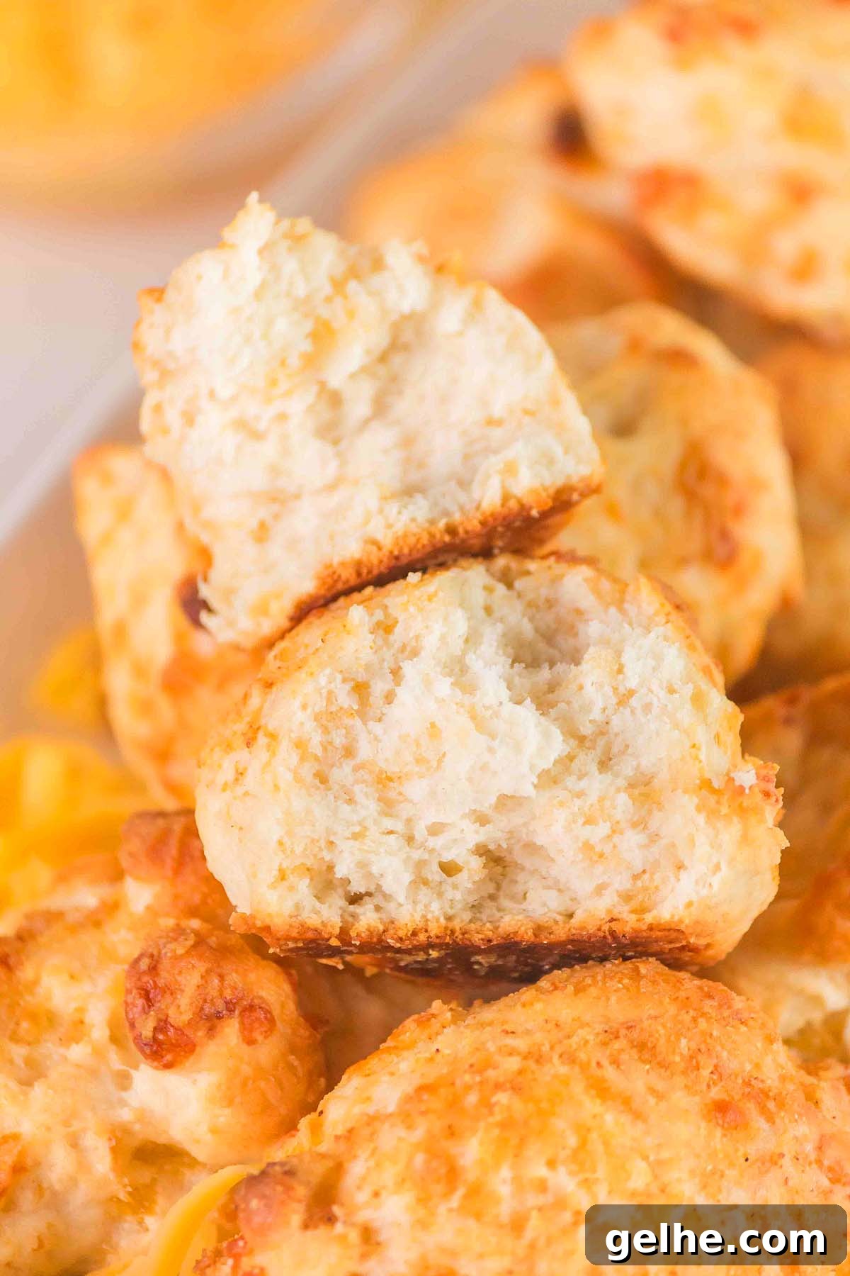 Flaky Cheddar Biscuits Made with Bisquick 8 Close-up of golden-brown Bisquick cheddar biscuits stacked on a plate, with one broken open to reveal a fluffy interior.