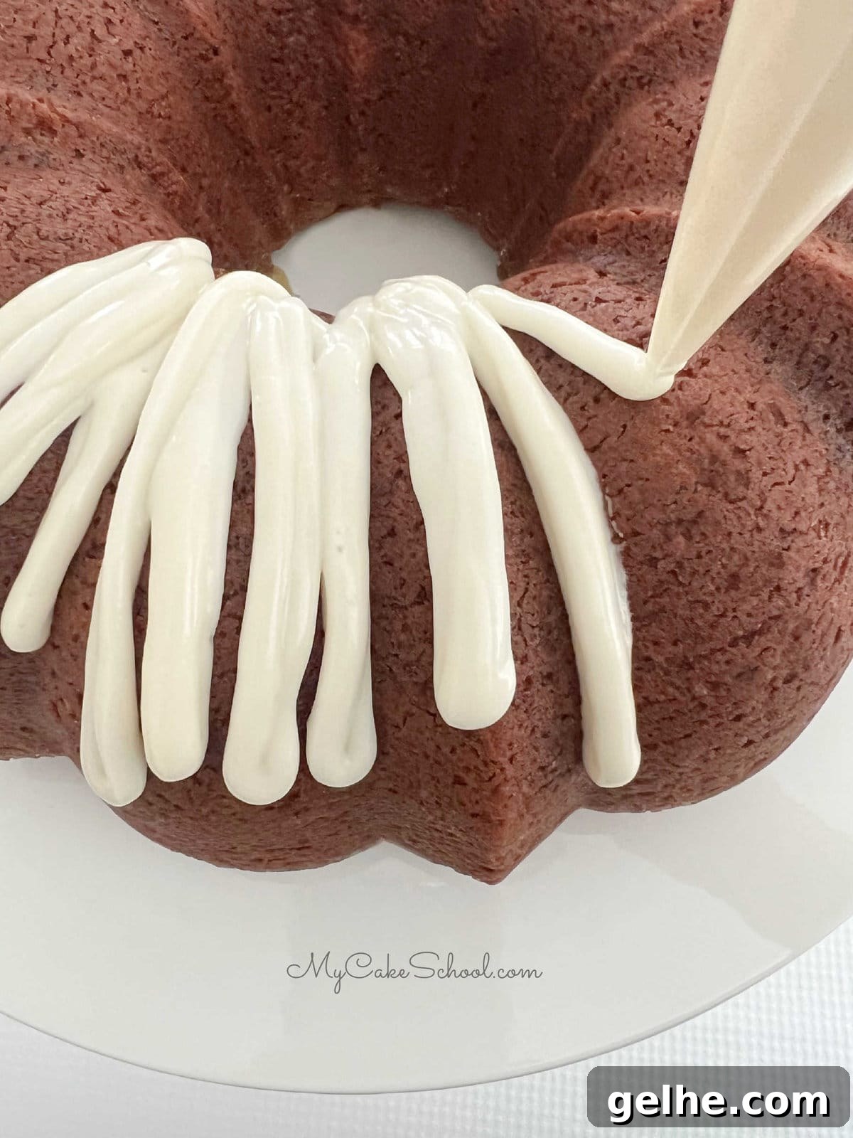 Piping cream cheese glaze onto the hummingbird bundt cake