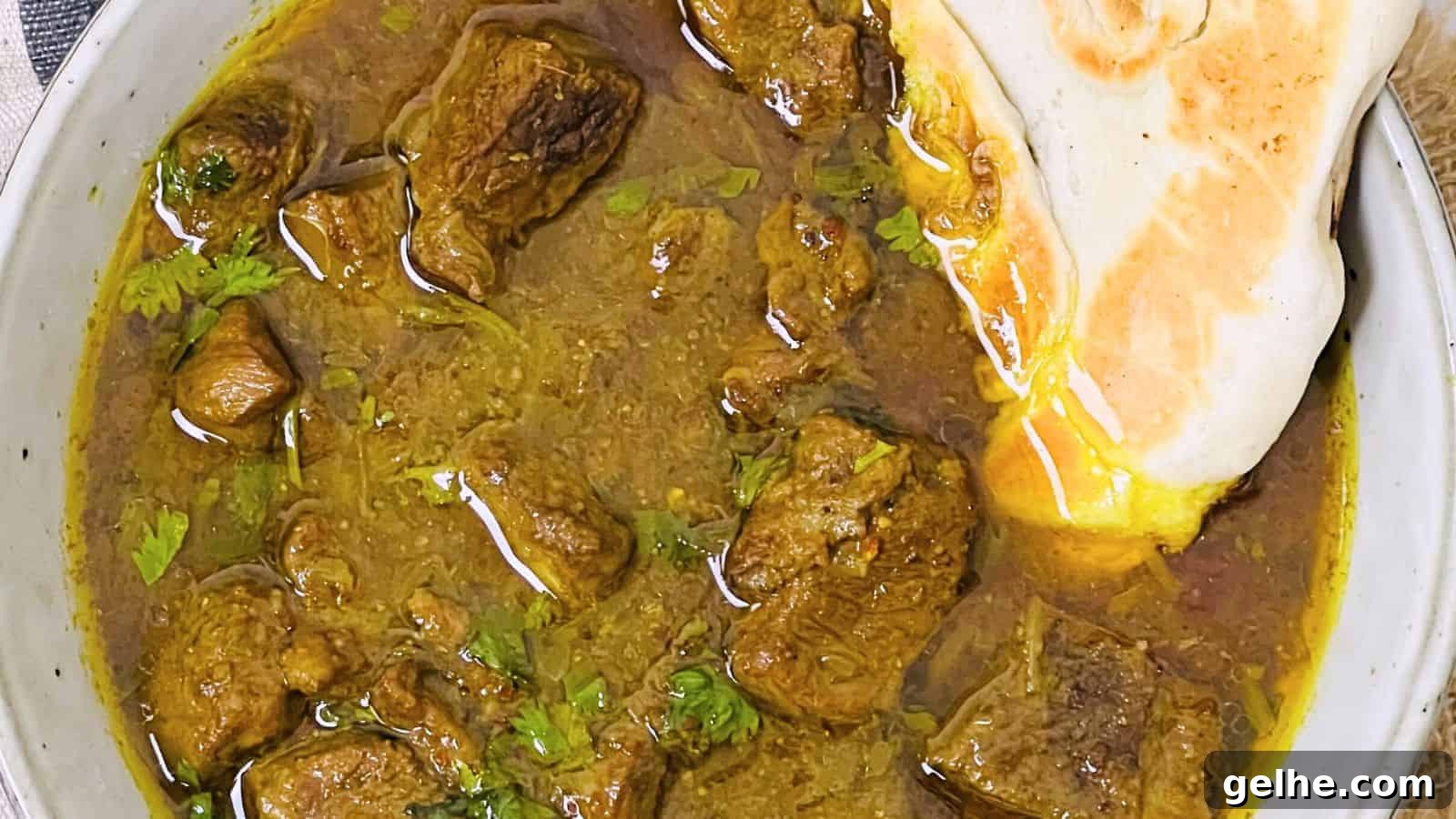 A bowl of rich beef curry garnished with cilantro, accompanied by a piece of naan bread partially dipped in the sauce.