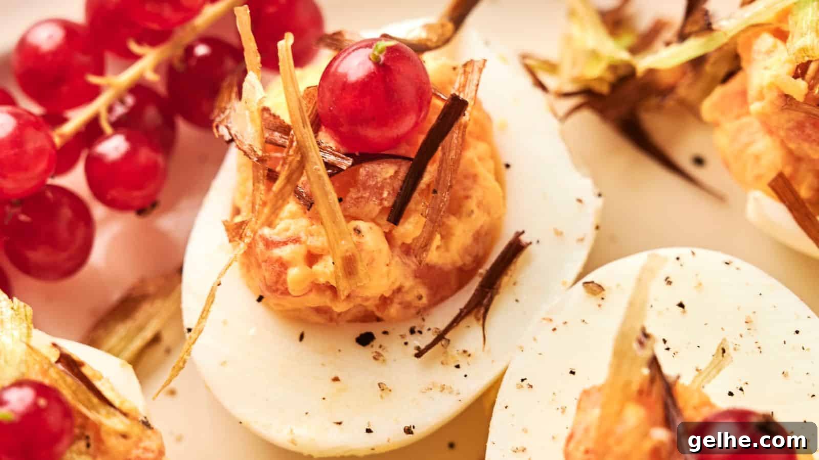 Close-up of Deviled Eggs topped with a red currant and garnished with fried leeks. Fresh red currants are in the background.