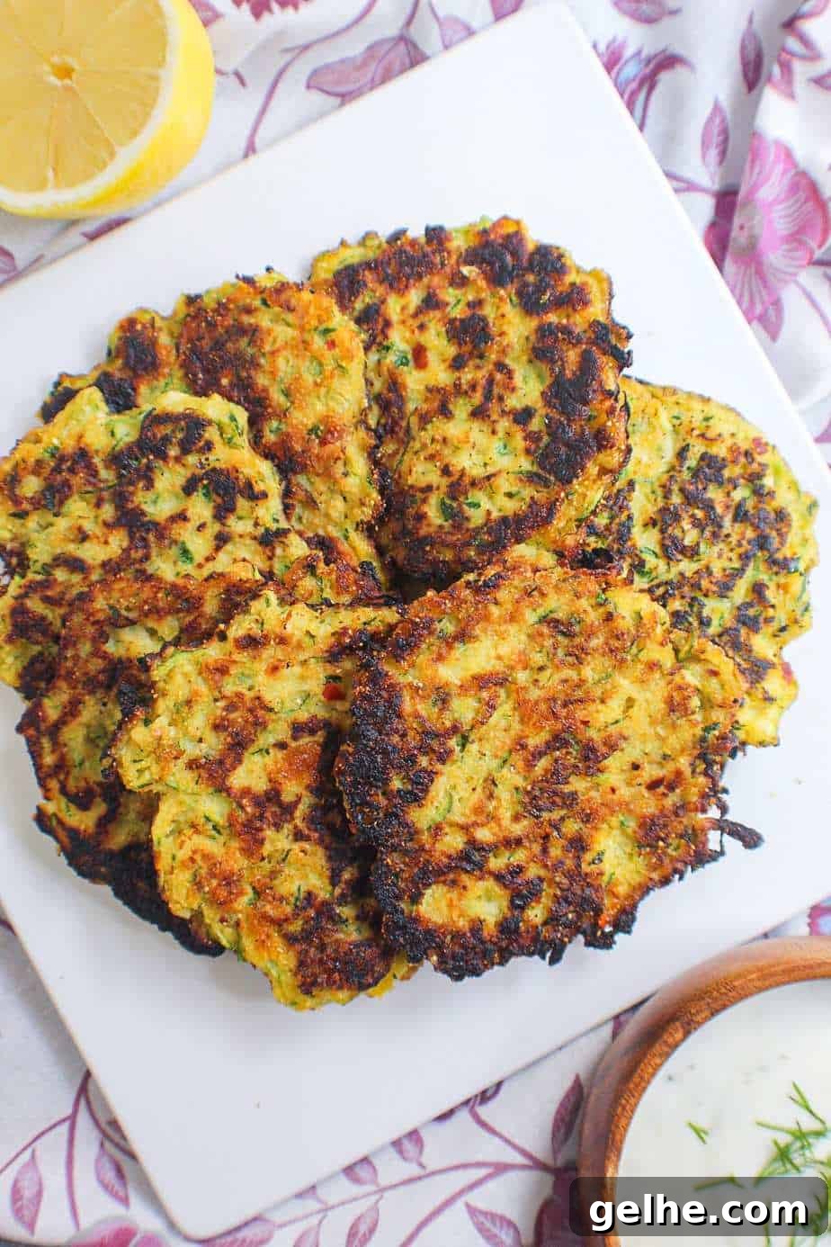 Crispy Cornmeal Zucchini Fritters with Garlic Herb Dip 2 overhead shot of cornmeal zucchini fritters on a white plate with yogurt dill dipping sauce in the bottom left corner.