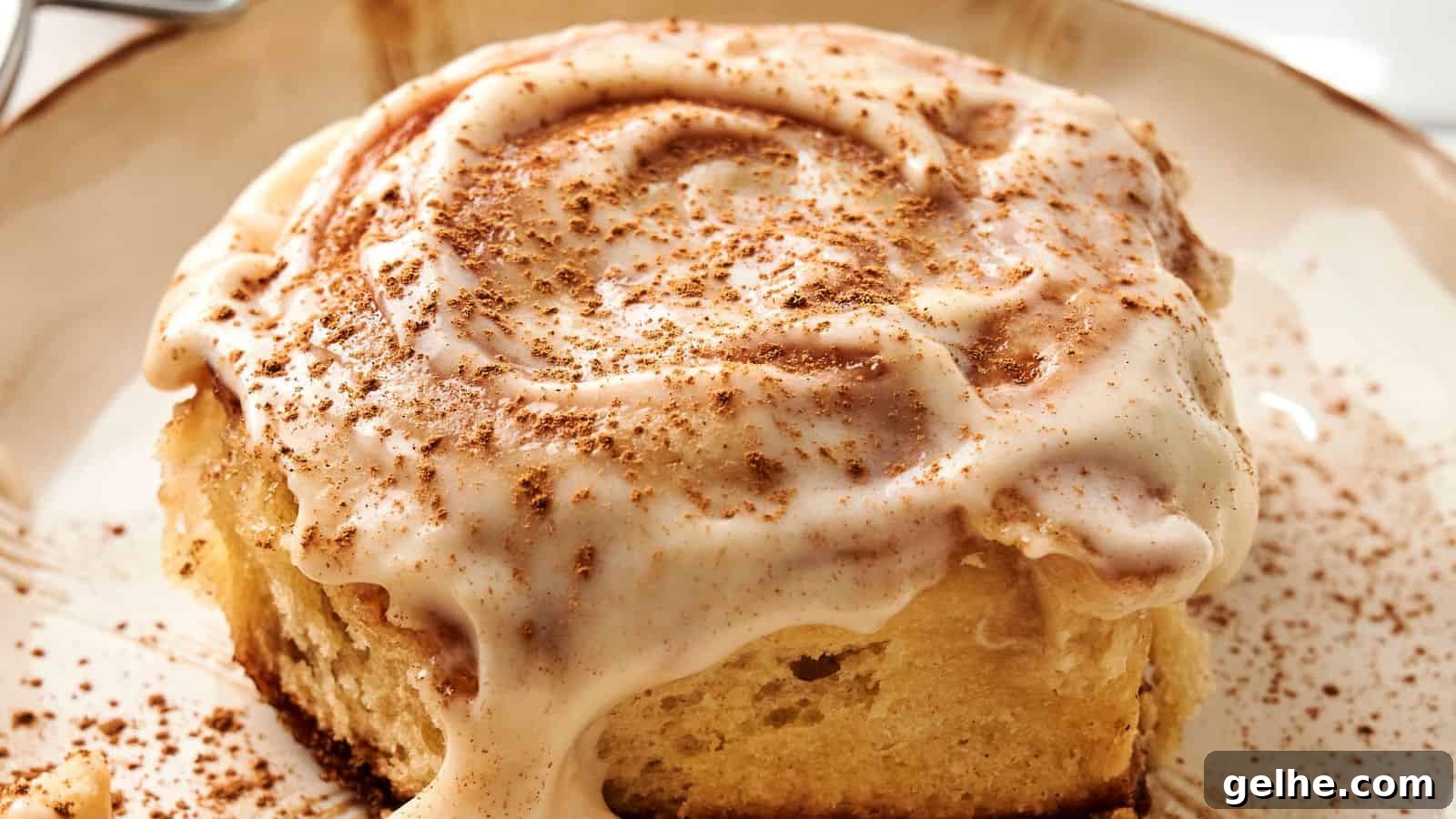 A close-up of a sourdough cinnamon roll topped with creamy icing and a sprinkle of cinnamon on a plate.