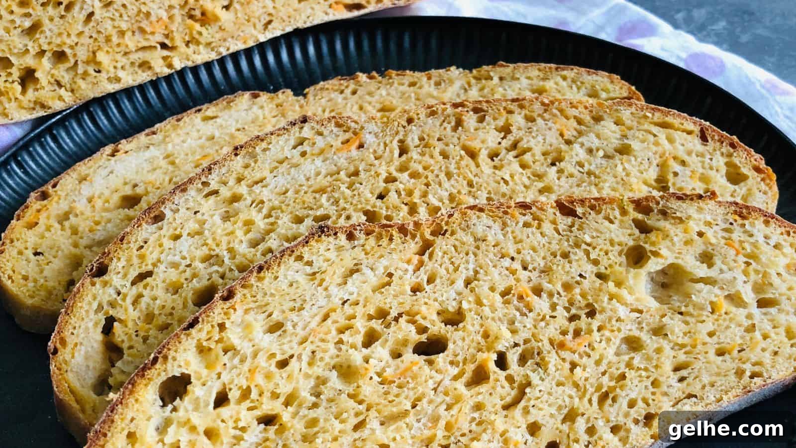A black plate holds four slices of rustic bread with a golden crust and airy interior, with additional slices visible in the background.