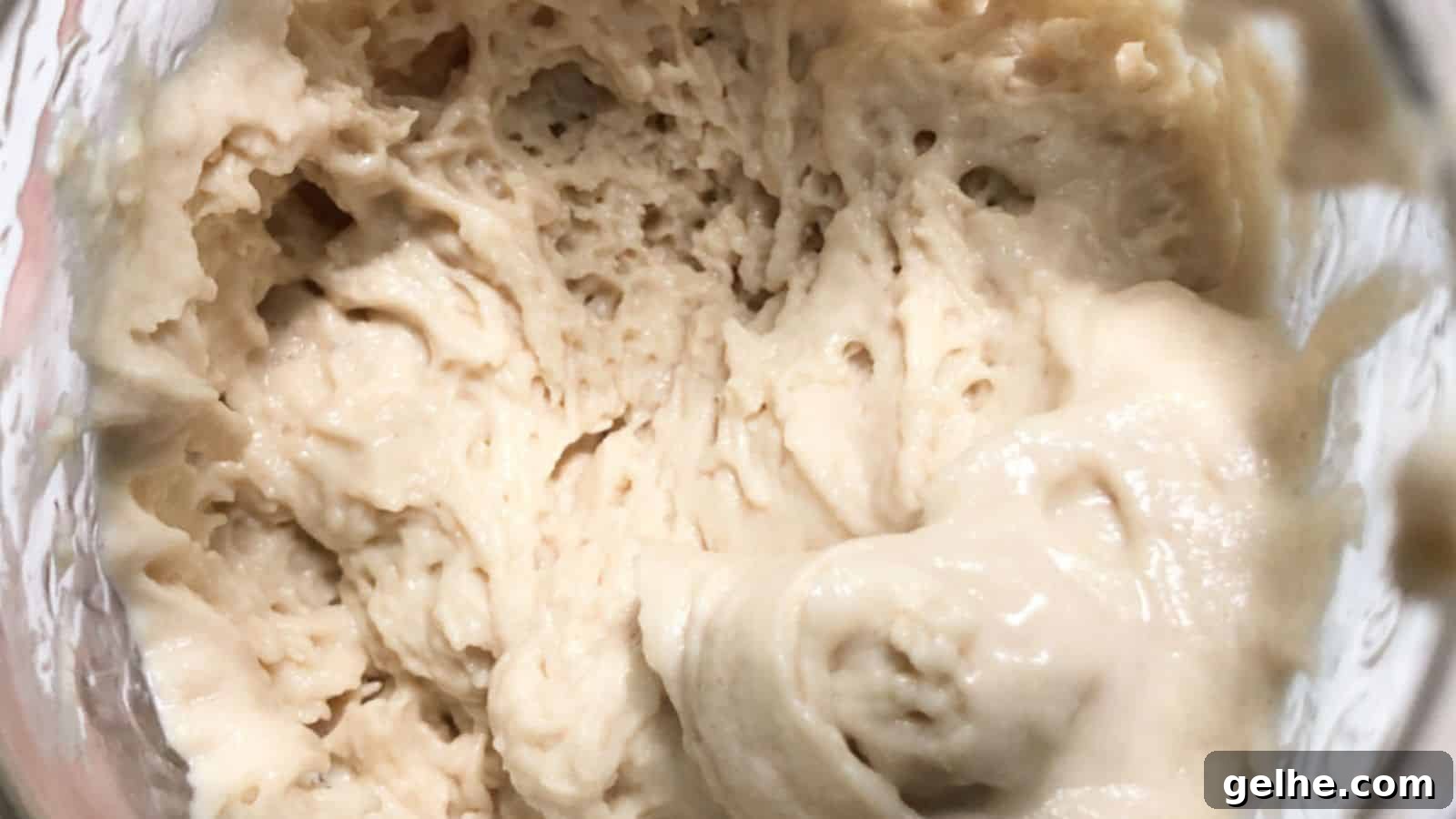 Close-up of creamy, beige-colored dough with an airy texture in a glass container.