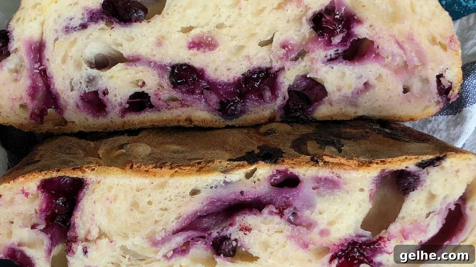 Close-up of two slices of freshly baked bread with visible blueberries and swirls of blueberry juice within the soft crumb. The crust appears lightly browned.