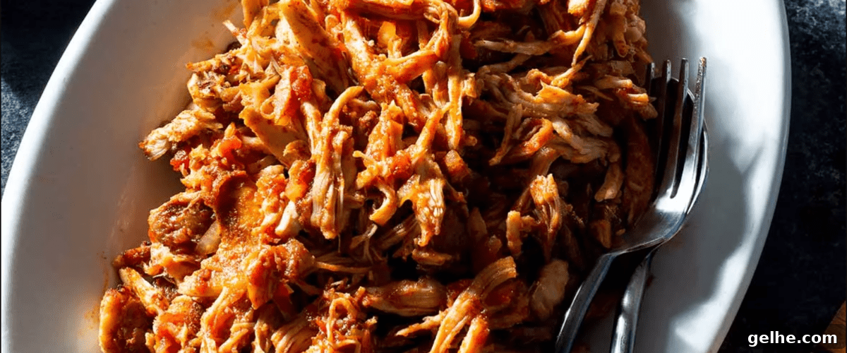 Oven pulled chicken thighs in white dish with fork.