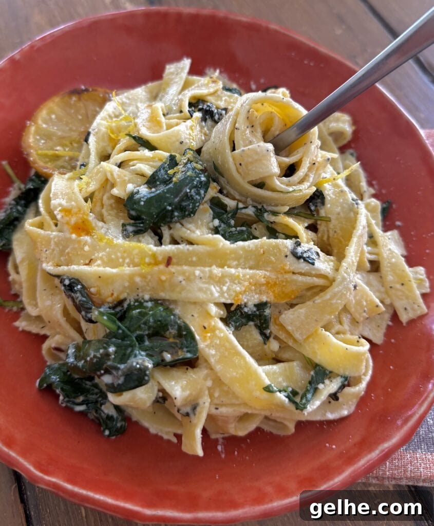 Twirling some creamy lemon tagliatelle on a fork in an orange pasta bowl.