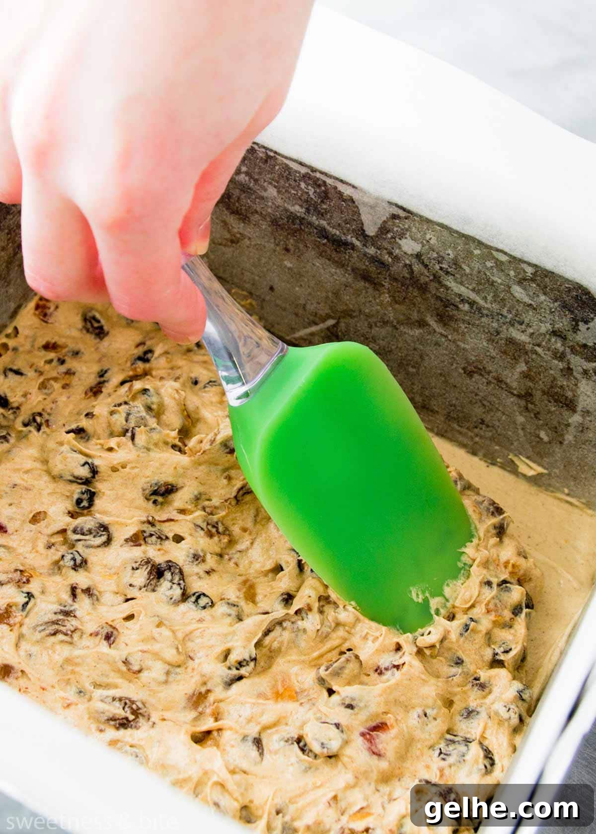 Christmas cake batter being pressed into the prepared cake pan with the back of a spatula.