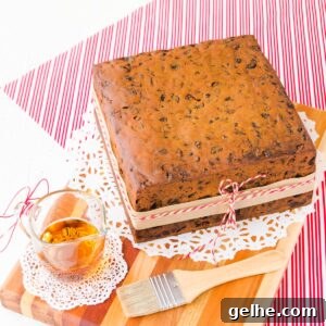 gluten free fruit cake on a wooden board, with a small glass jug of brandy and a pastry brush.