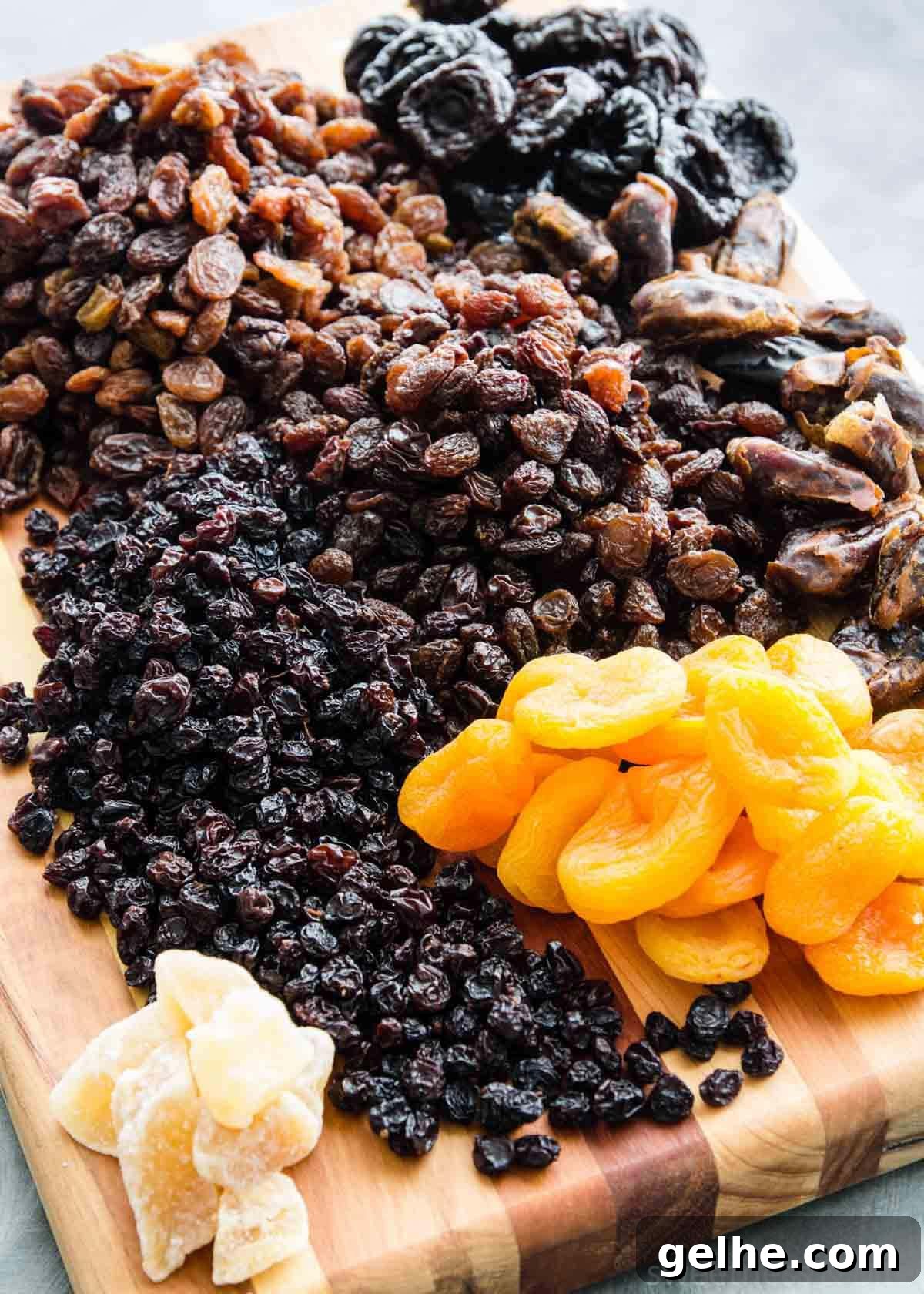 Dried fruits - sultanas, raisins, dates, prunes, currants, apricots and glacé ginger - on a wooden board.