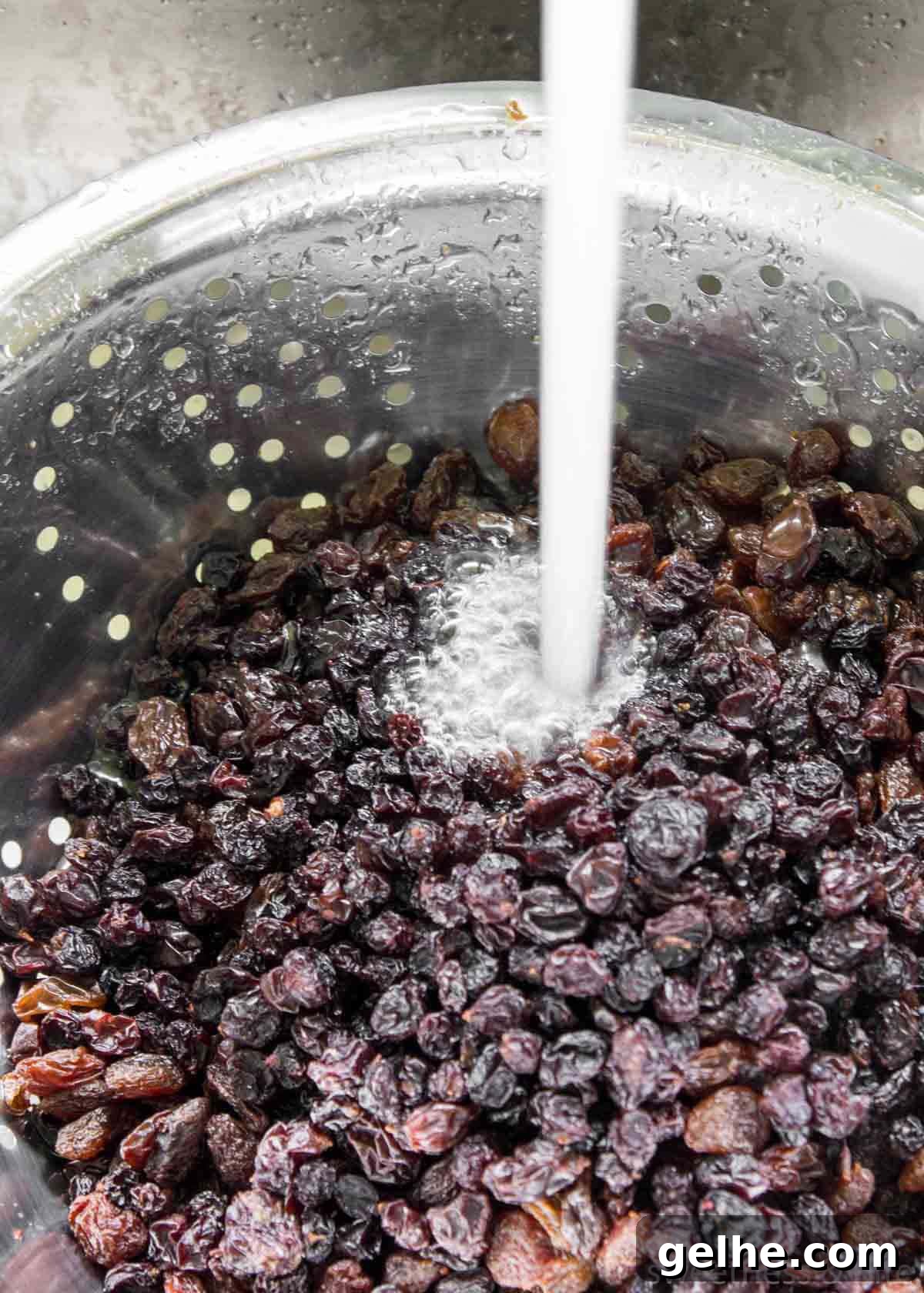 Raisins being rinsed under a tap in a metal colander.