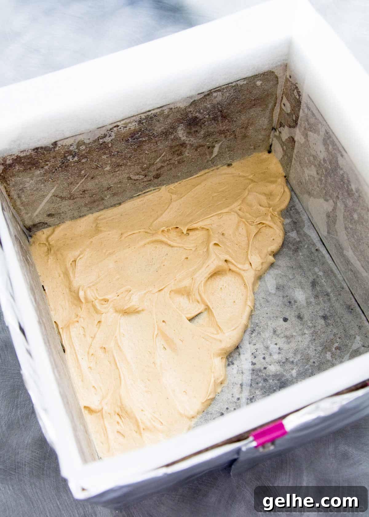 A square cake pan lined with baking paper, with cake batter spread over the bottom.