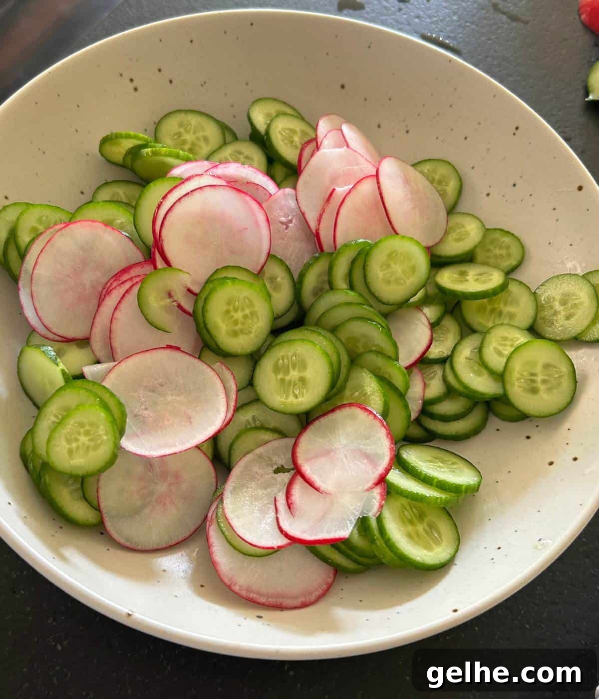 Thinly sliced radish and cucumbers in bowl.