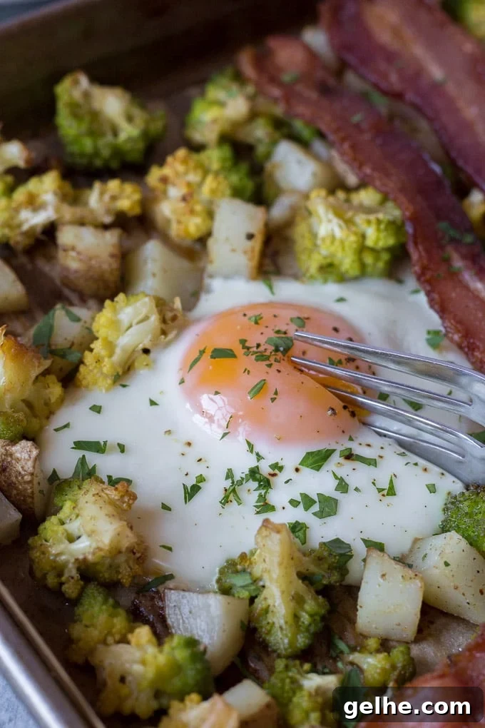 Whole30 Sheet Pan Breakfast Bake for Busy Mornings 3 shot of a silver fork cutting into a cooked egg on a sheet pan with potatoes, romanesco, and bacon