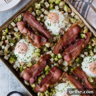top down view of easy sheet pan breakfast with eggs, bacon, potatoes, and romanesco. Surround by white plates with forks, a striped white and blue towel, and a silver spatula