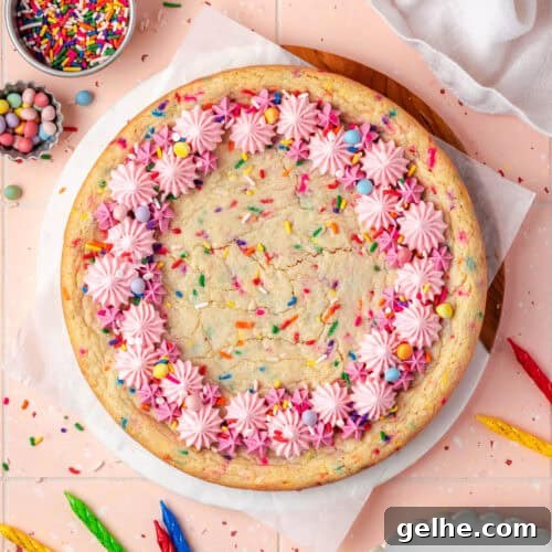 A sugar cookie cake decorated with pink frosting and sprinkles sitting on a pink tile table.
