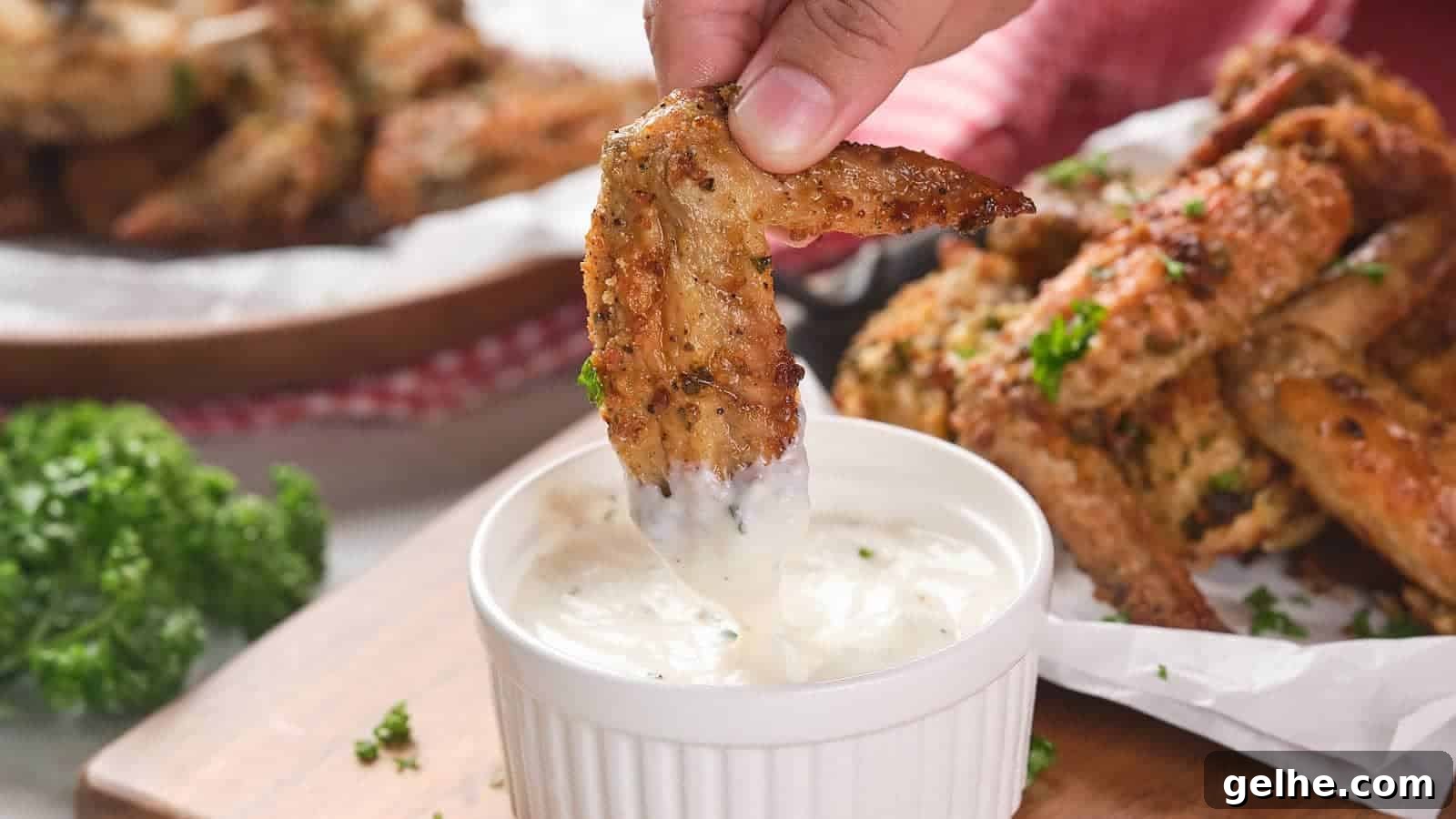 21 Labor Day Picnic Recipes for a Crowd: Ultimate Menu Ideas 18 A hand dips a parmesan chicken wing into a small ramekin filled with white dipping sauce.