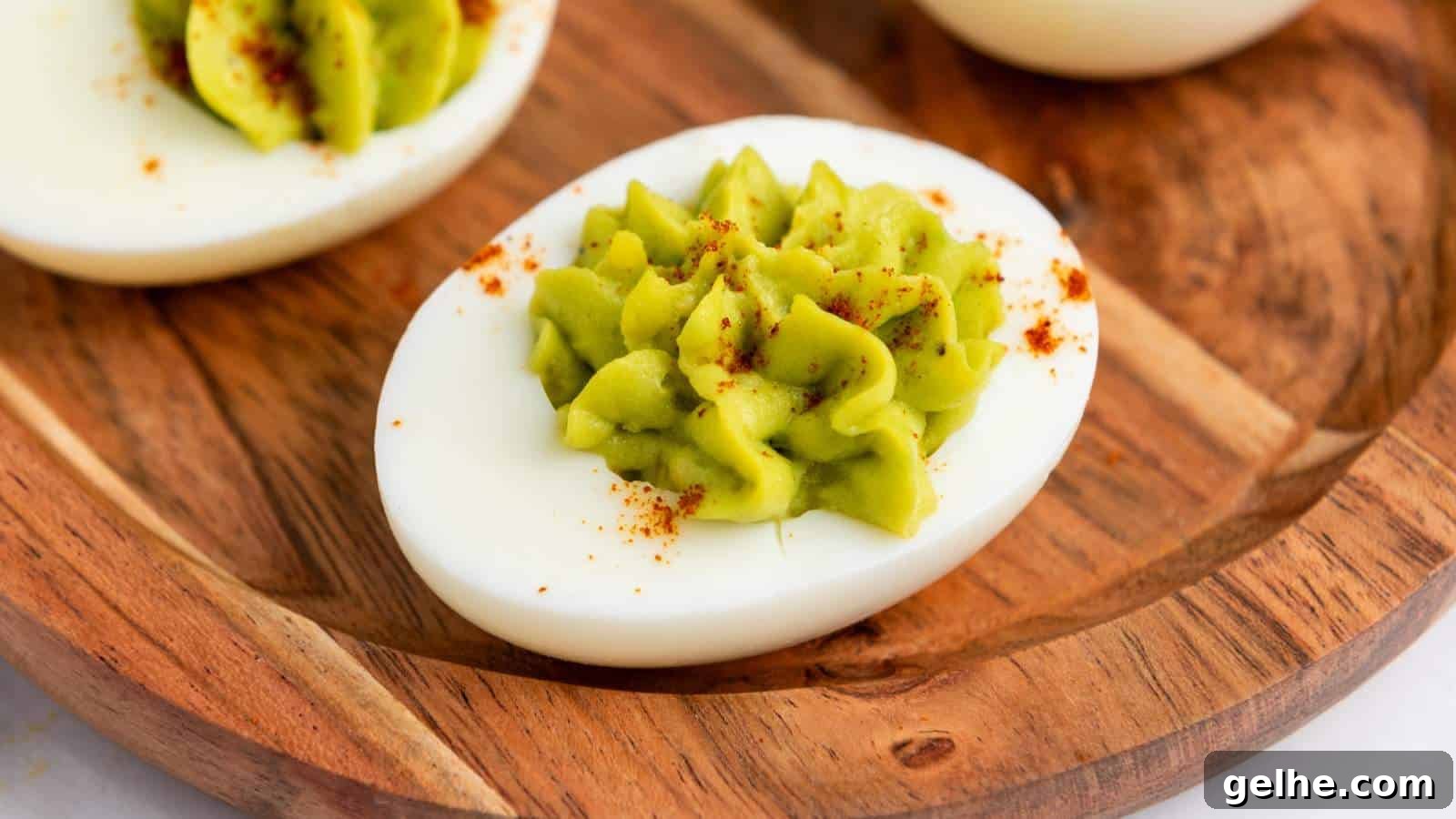 21 Labor Day Picnic Recipes for a Crowd: Ultimate Menu Ideas 20 Avocado deviled egg with green filling and a sprinkle of paprika on a wooden plate.