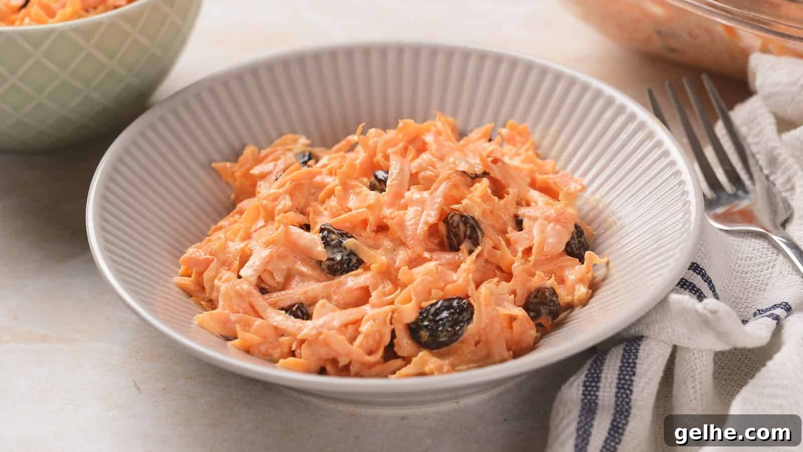 21 Labor Day Picnic Recipes for a Crowd: Ultimate Menu Ideas 7 A bowl of carrot raisin salad with a creamy dressing in a white ridged bowl, placed on a light surface.