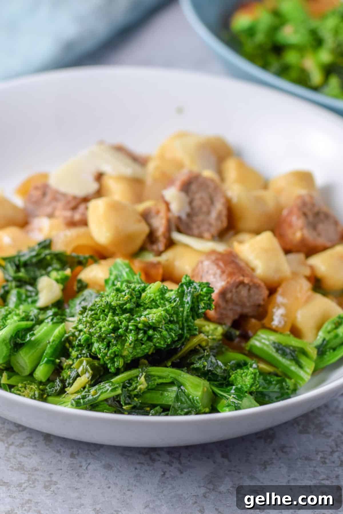 Close view of a white dish with gnocchi and sausage with broccoli rabe in the front