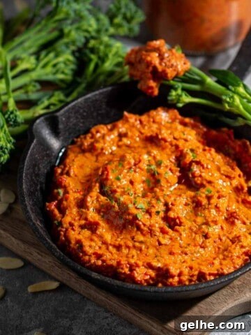 Romesco dip in a small black pan surrounded by broccoli spears, with a bottle of sauce in the background.