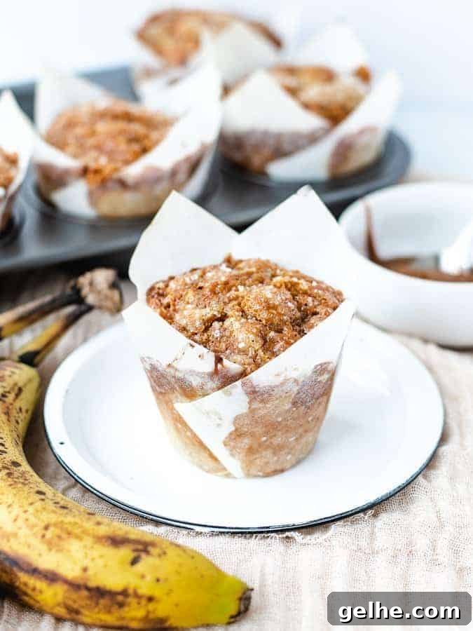 Banana muffin on a plate with pan of muffins behind and banana and dulce de leche off to the sides
