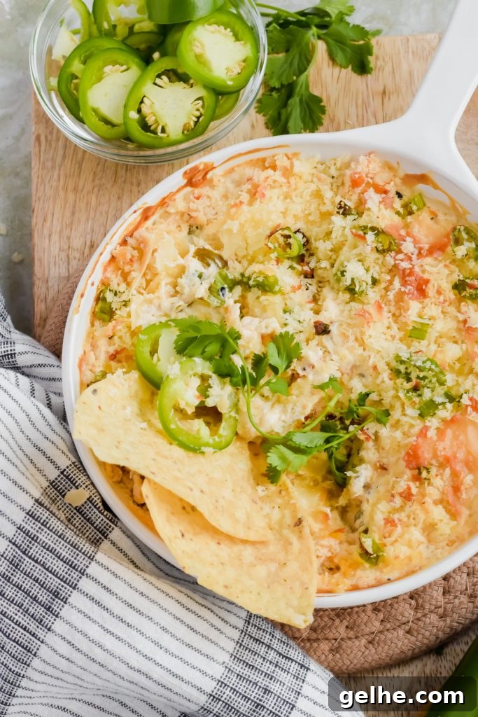 Baked Cheddar Jalapeño Dip with Crispy Panko Topping 7 Baked cheddar jalapeño dip in white skillet garnished with jalapeño slices and two tortilla chips stuck in on wood cutting board.