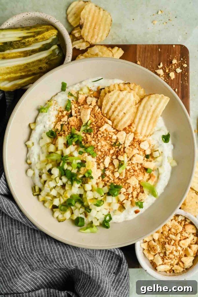 Baked Cheddar Jalapeño Dip with Crispy Panko Topping 8 fried pickle dip in serving bowl garnished with crushed crackers, green onion, and chopped pickles.