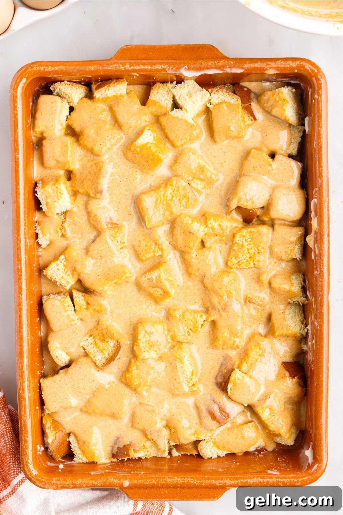 Pouring the mixture over the bread cubes in the baking dish.