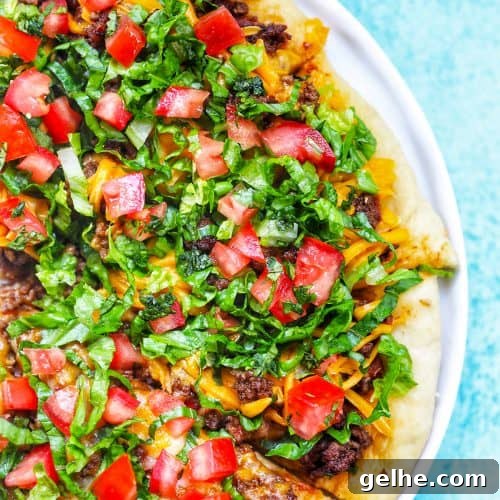 homemade taco pizza on a white plate and blue background.