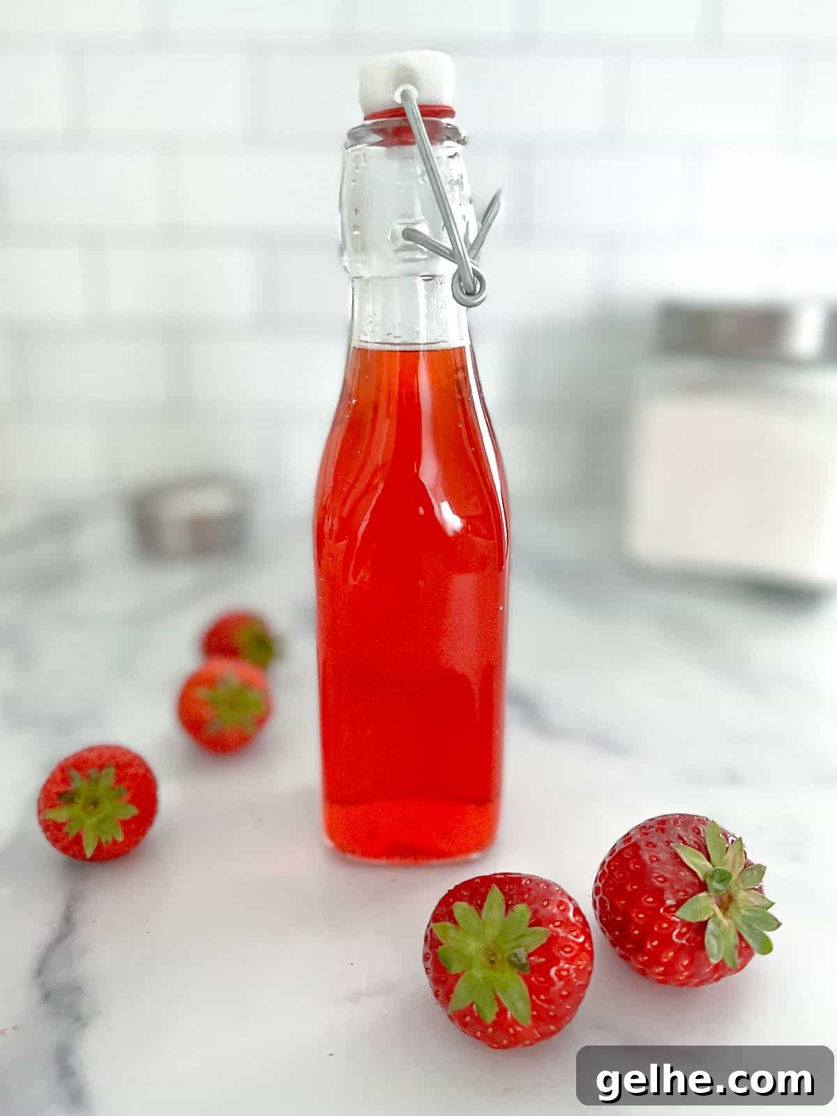 Homemade strawberry simple syrup in a glass bottle with strawberries on ground.