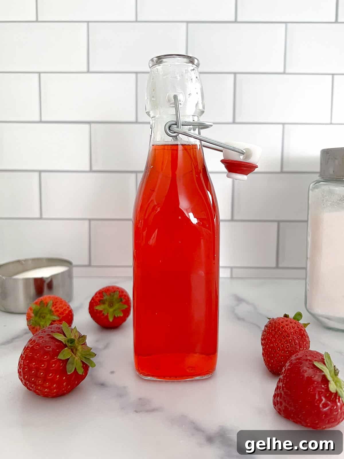 Homemade strawberry simple syrup in a glass bottle with open lid and sugar on the side.