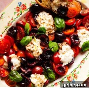 A colorful caprese salad with tomatoes, cherries, mozzarella, and basil on a decorative platter.