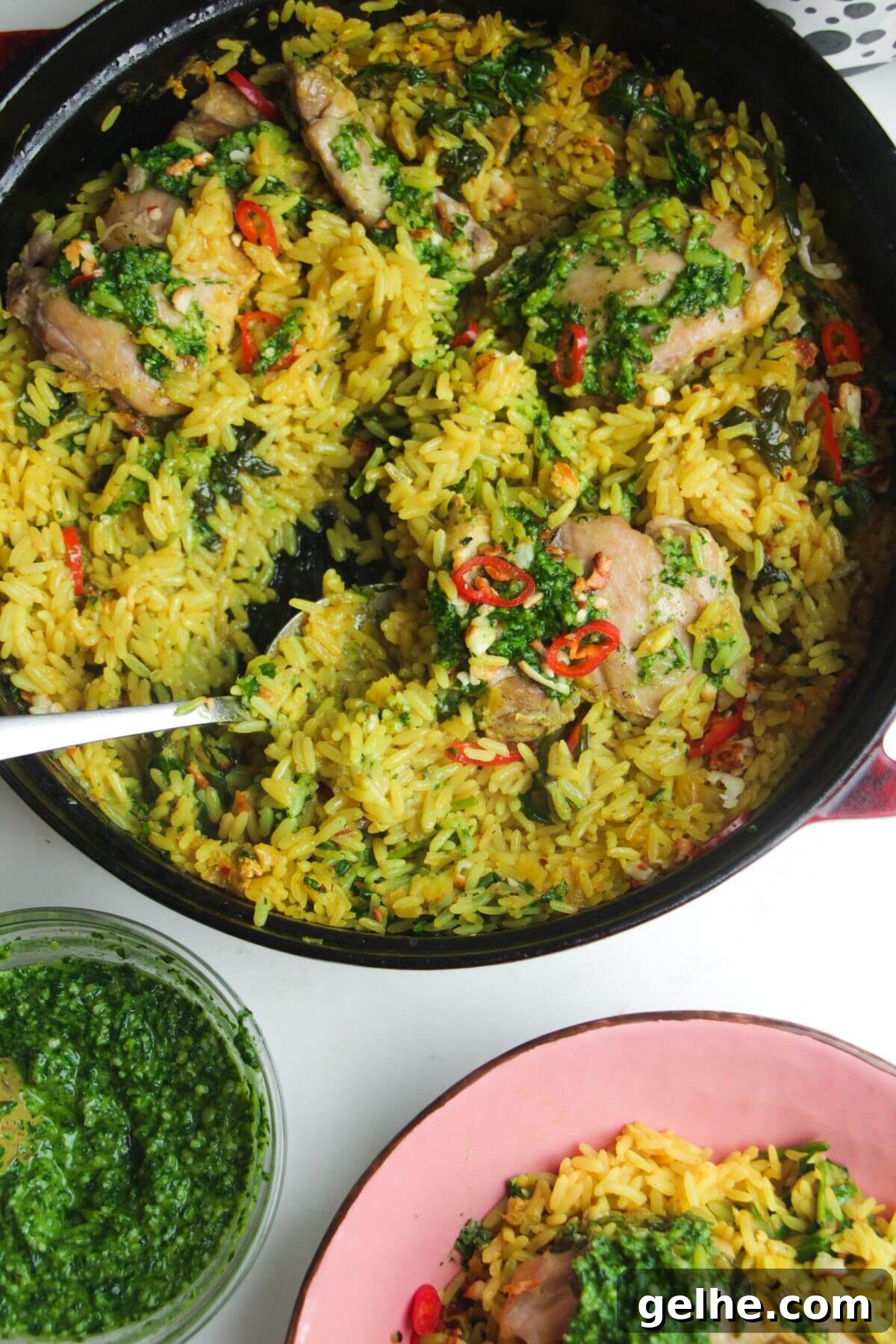 Pesto topped chicken with rice in a large pot with pink plate and pesto on the side.