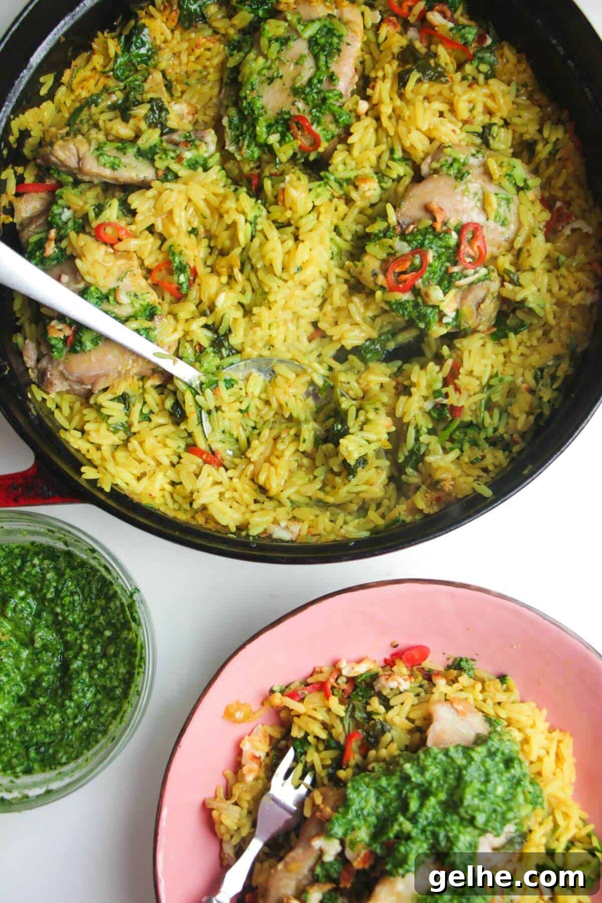 Pesto topped chicken with rice in a large pot with pink plate and pesto on the side.