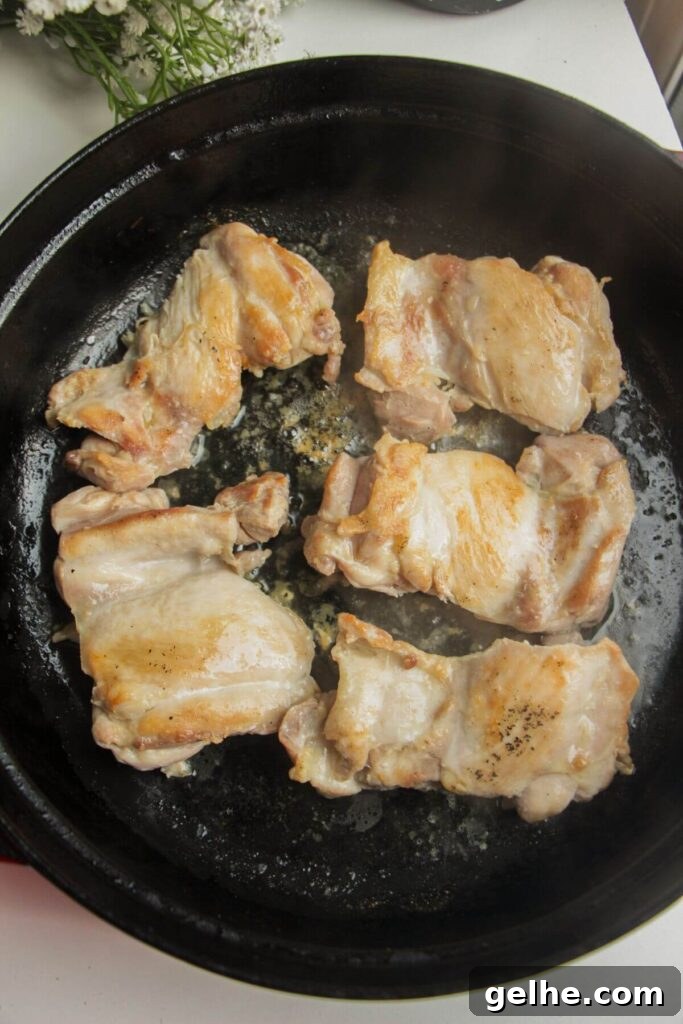 Chicken thighs cooking in a large pan.