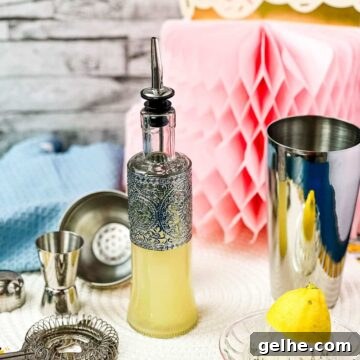 Bottle filled with freshly squeezed lemon juice fitted with a pouring spout, surrounded by cocktail making tools.
