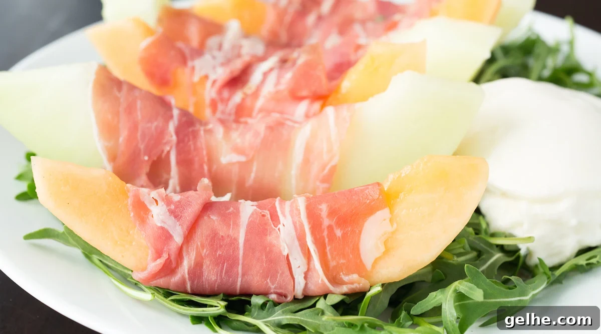 Prosciutto, Melon & Burrata Salad with Honey-Lemon Dressing 2 Alternating slices of cantaloupe and honeydew melon that are wrapped with prosciutto. They are sitting on a bed of arugula next to a ball of burrata.