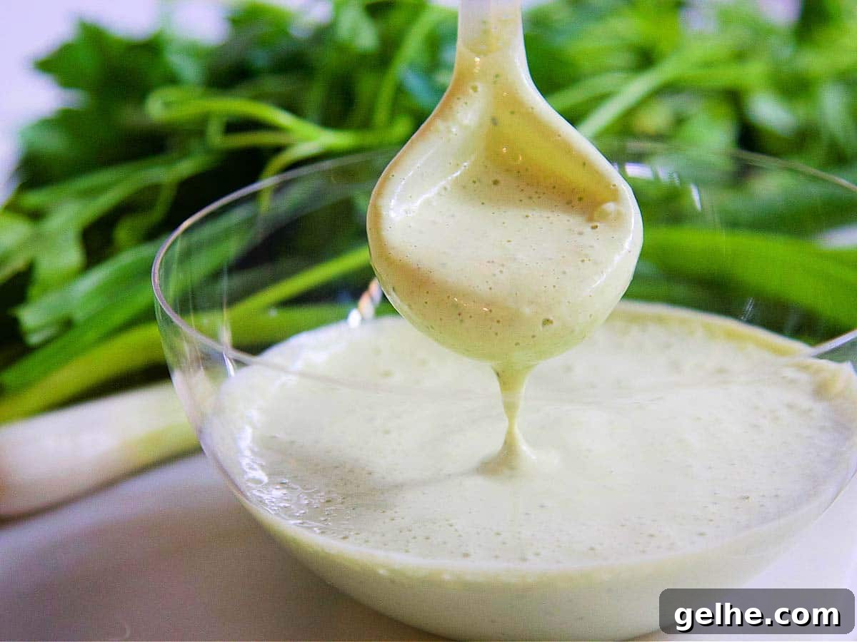 A clear glass bowl with a spoon dipping into Green Goddess dressing.