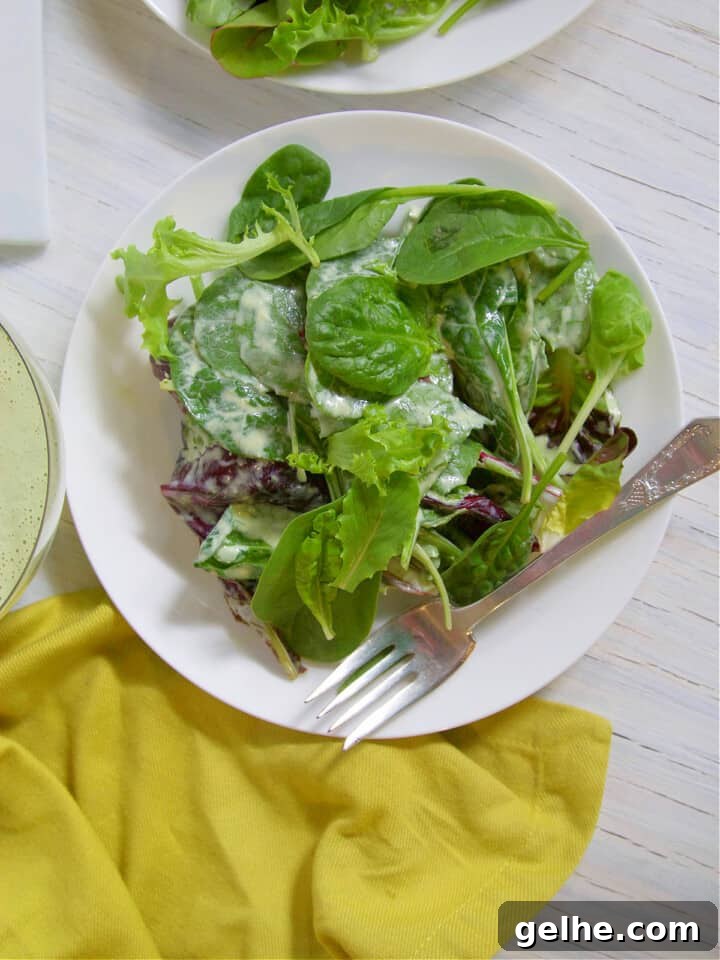 Small white plate with silver fork and greens tossed in green goddess salad dressing.