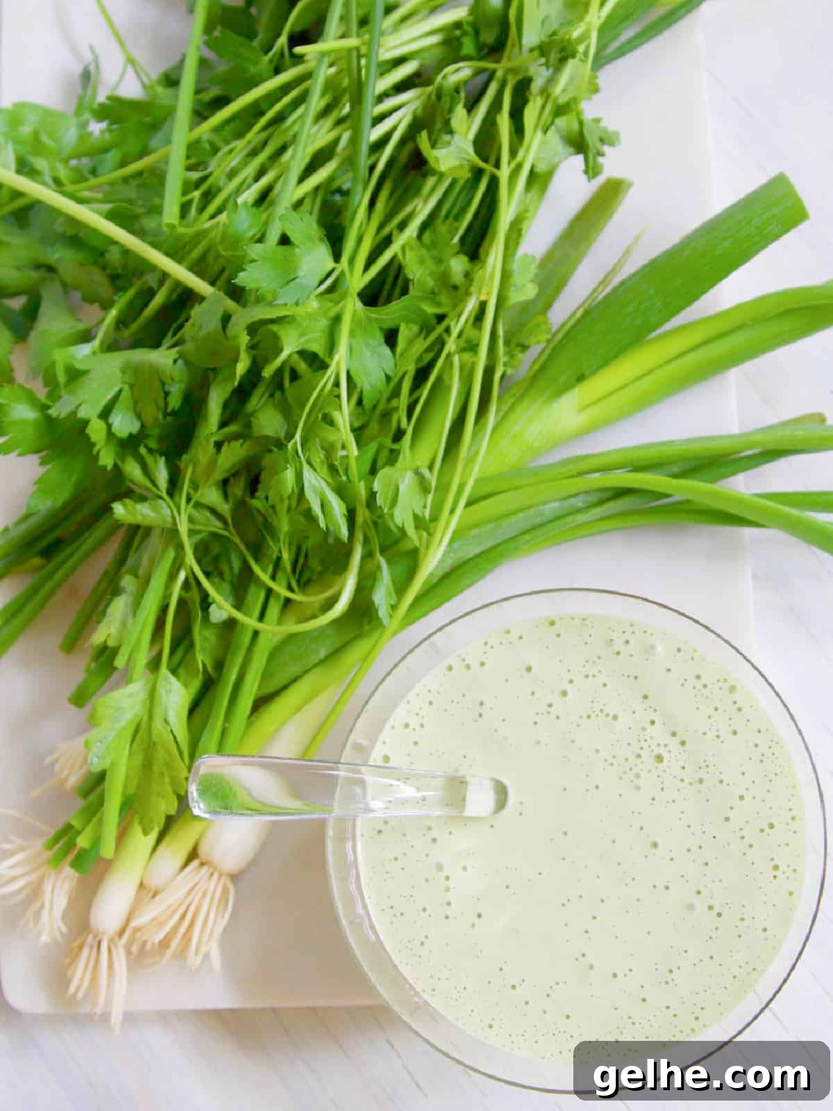 Clear glass bowl with glass spoon and a pile of green onions and parsley.