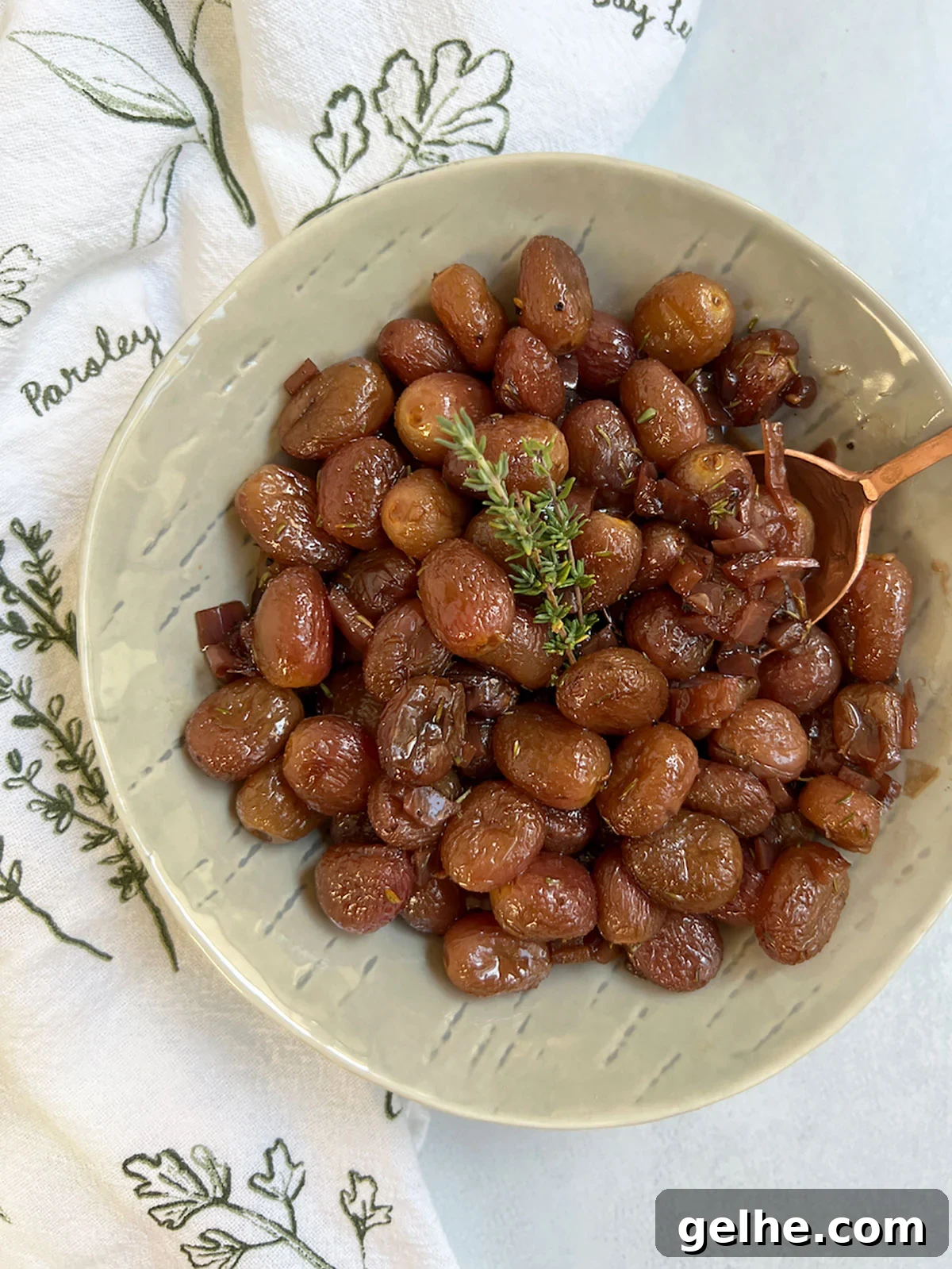 Roasted grapes in a grey bowl with an herby napkin and copper spoon.