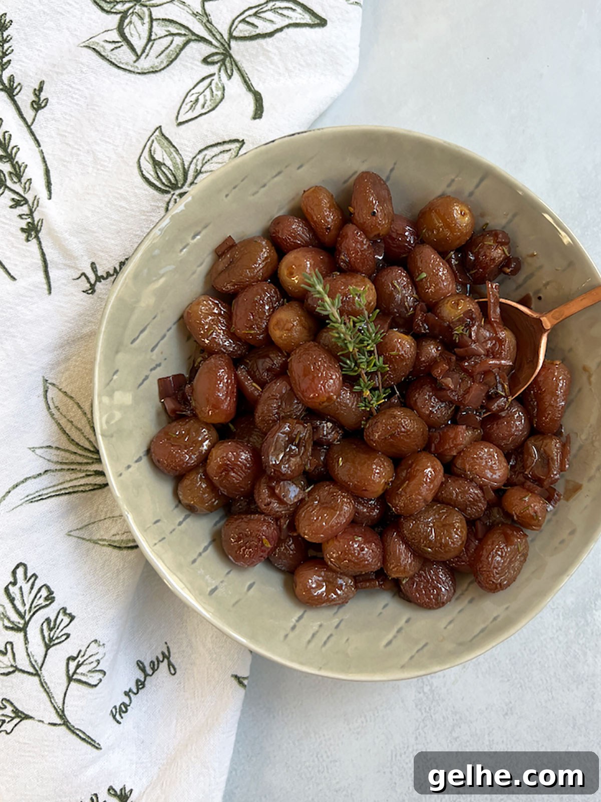 Roasted grapes in a bowl with a copper spoon.