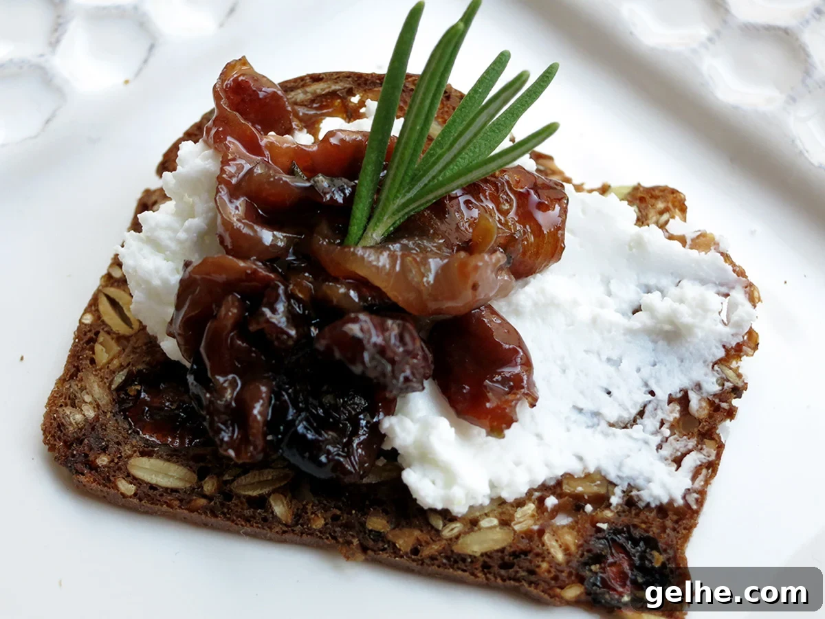 Roasted grapes and goat cheese on a fig cracker with a sprig of rosemary on top.