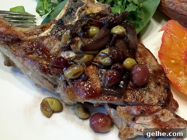 Pork chop on a white plate with roasted grapes on top.
