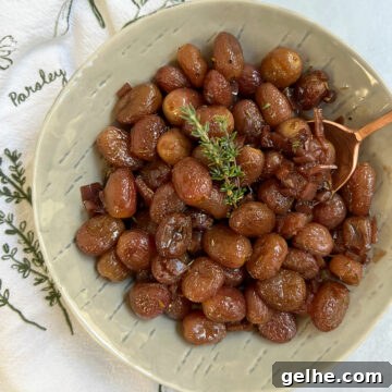 Roasted grapes in a grey bowl with an herby napkin and copper spoon.