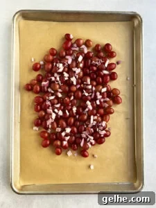 Uncooked grapes and shallots on a parchment-lined baking sheet.