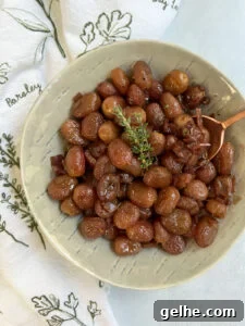 Roasted grapes in a grey bowl with an herby napkin and copper spoon.