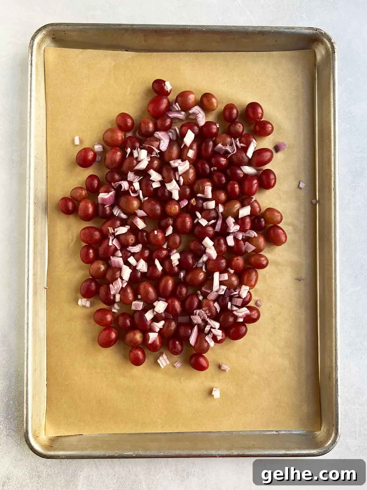 Uncooked grapes and shallots on a parchment-lined baking sheet.