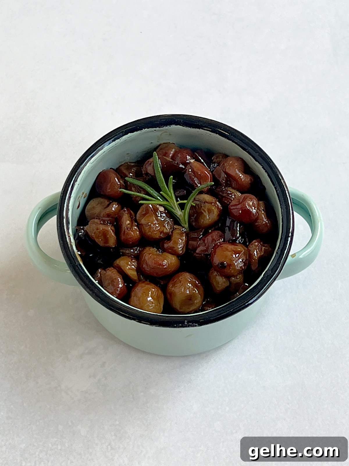 Roasted grapes in a turquoise serving bowl with rosemary on top.